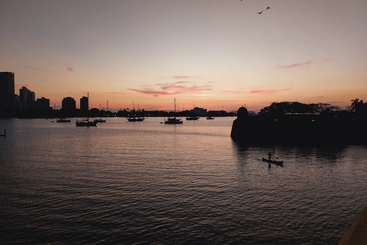 Cartagena Bay at dusk, with a pink sky, moored sailboats and the dark outline of the shore.